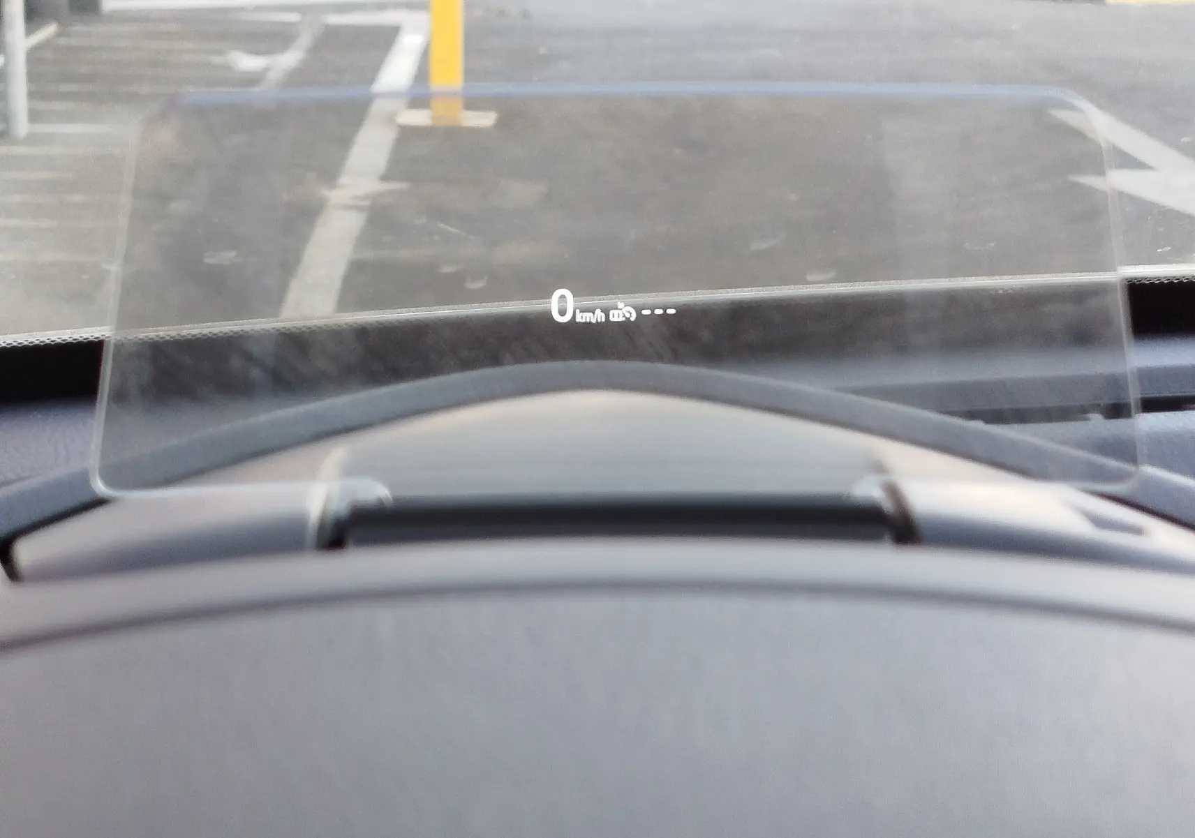 Affichage tête haute transparent montrant la vitesse à 0 km/h dans le tableau de bord d'une Mazda2 blanche.