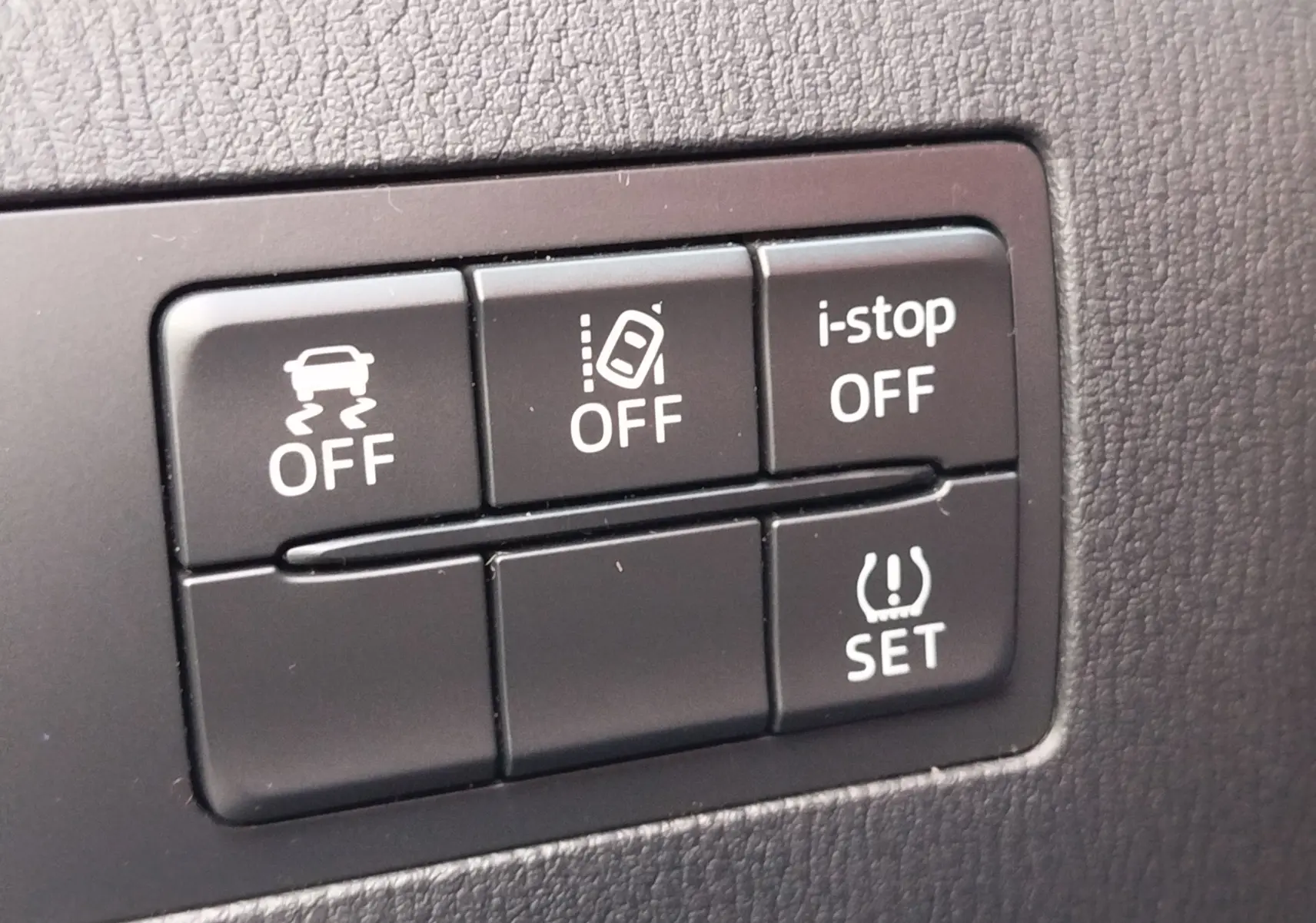 Gros plan sur les boutons de contrôle du tableau de bord d'une Mazda2 2018, finition noire mate.