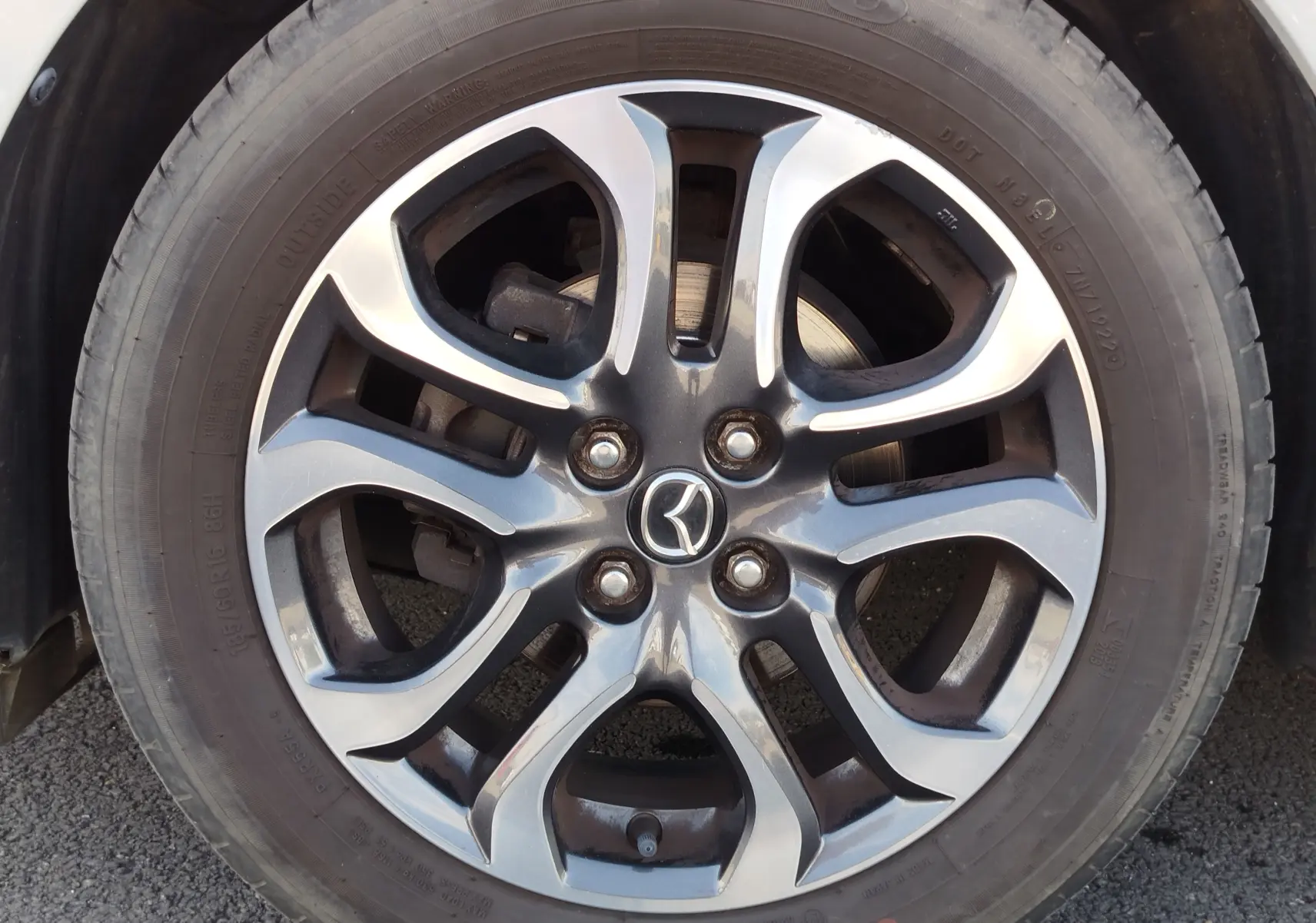 Gros plan sur la jante alliage bi-ton de la Mazda2 blanche, mettant en valeur le logo Mazda au centre.