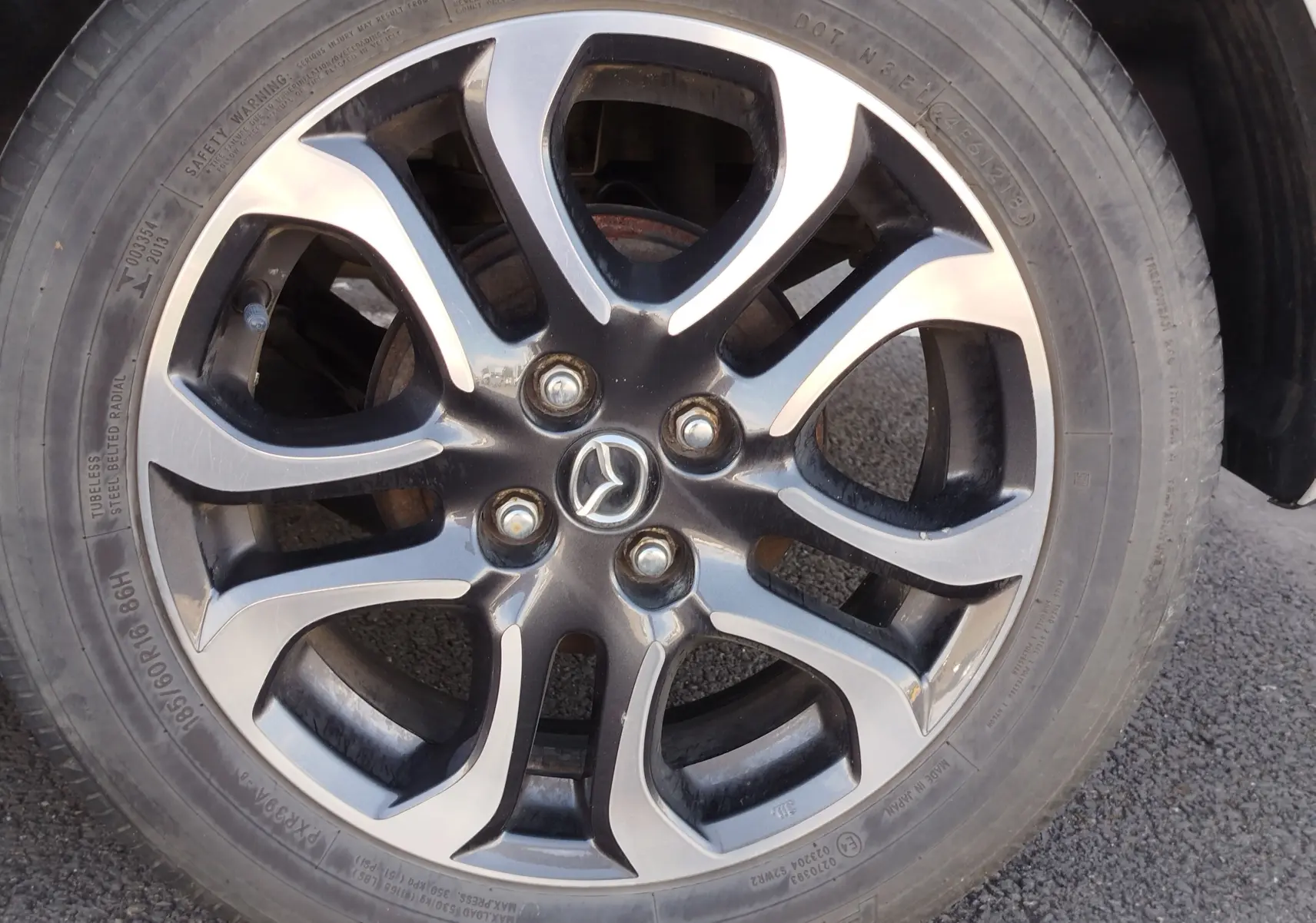 Gros plan sur la jante alliage bi-ton noir et argent avec logo Mazda, roue avant droite d'une Mazda2 blanche.