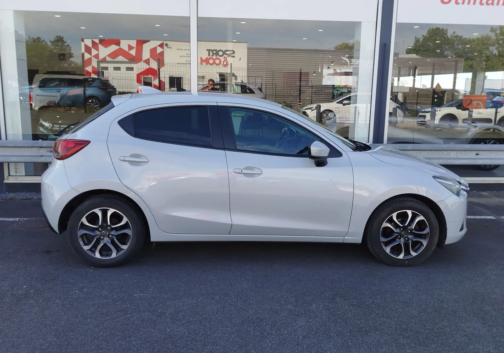 Vue latérale droite d'une Mazda2 blanche nacrée 2018, avec jantes alliage bicolores et vitres teintées.