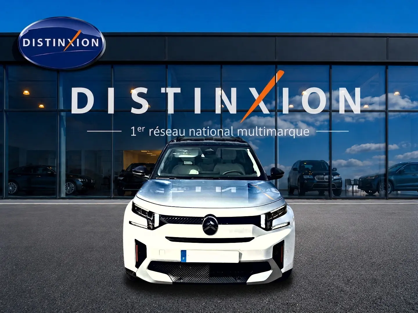 Vue frontale d'un Citroën C3 Aircross blanc 2026 avec calandre noire et toit panoramique, devant un showroom Distinxion.
