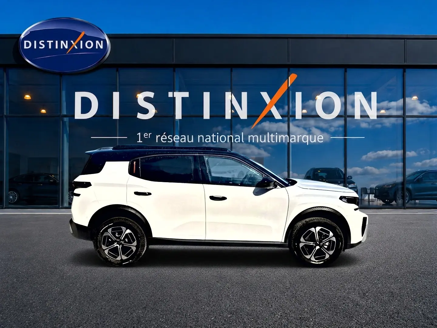 Profil droit d'un Citroën C3 Aircross blanc 2026 avec toit noir, jantes alu et vitres teintées, devant une vitrine Distinxion.