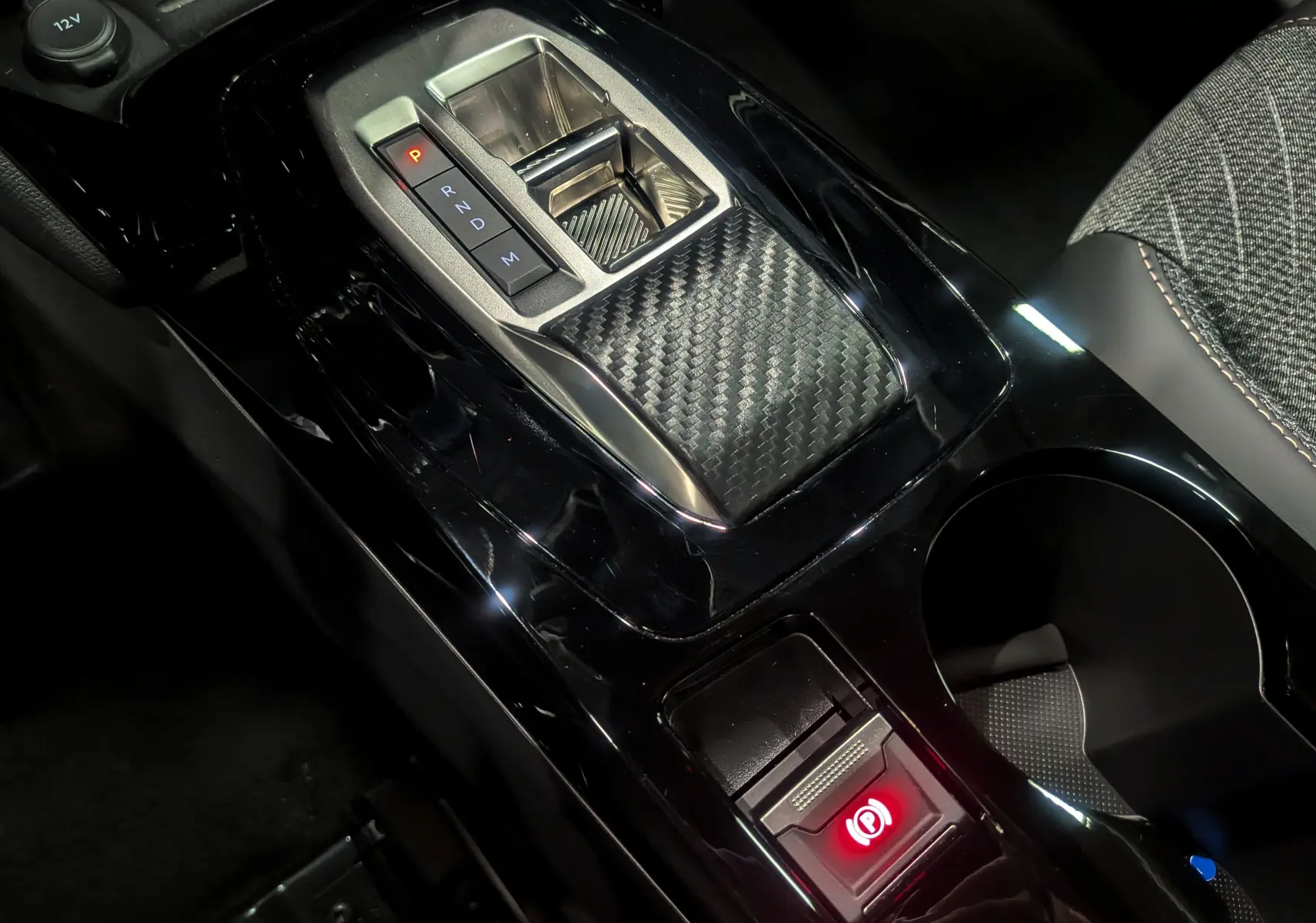 Vue rapprochée de la console centrale noire brillante du Peugeot 2008 Hybrid 145 avec levier de vitesses automatique et frein à main électronique.
