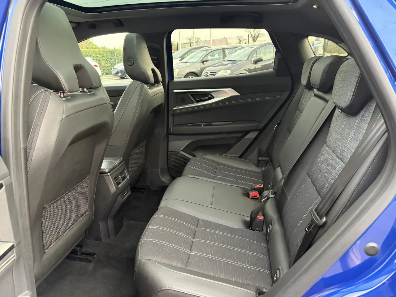 Vue intérieure arrière côté gauche du Renault Austral bleu Iron, montrant la banquette mixte tissu et cuir gris et les dossiers des sièges avant.