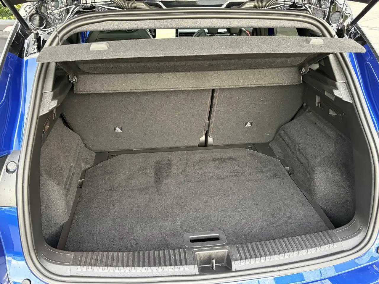 Coffre ouvert vu de l'arrière d'un Renault Austral bleu Iron avec intérieur de coffre noir et cache-bagages relevé.