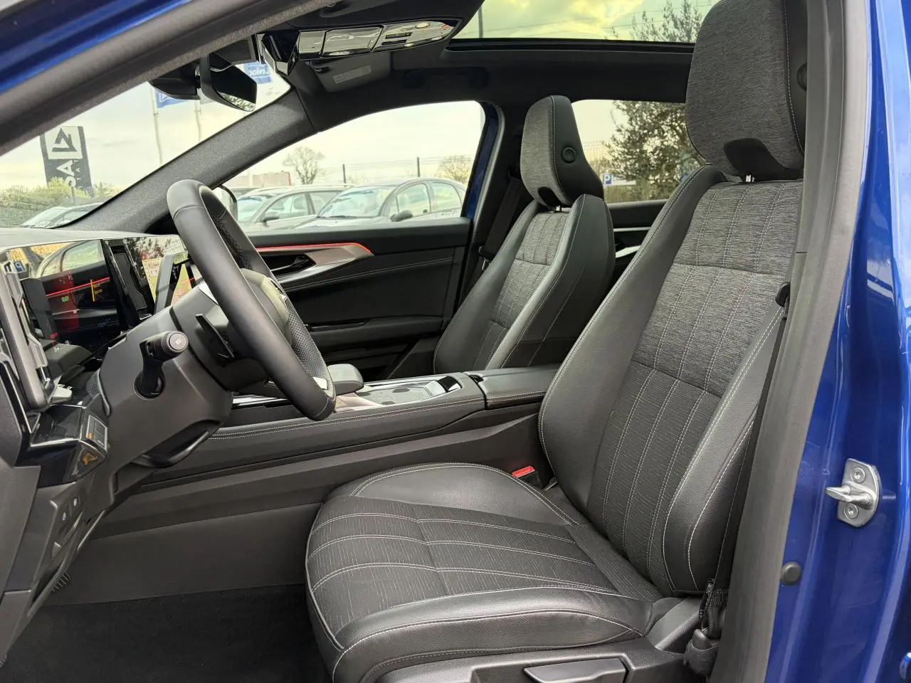 Vue intérieure côté conducteur du Renault Austral E-Tech bleu Iron, avec sièges gris tissu et toit panoramique visible.