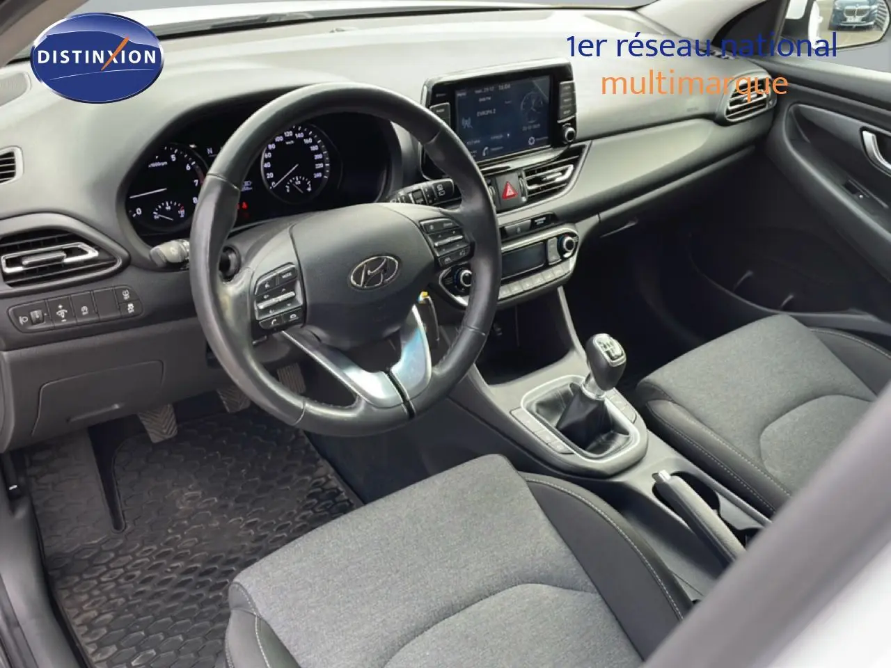 Vue intérieure côté conducteur de la Hyundai i30 SW 2022, volant cuir multifonction et sellerie tissu gris.