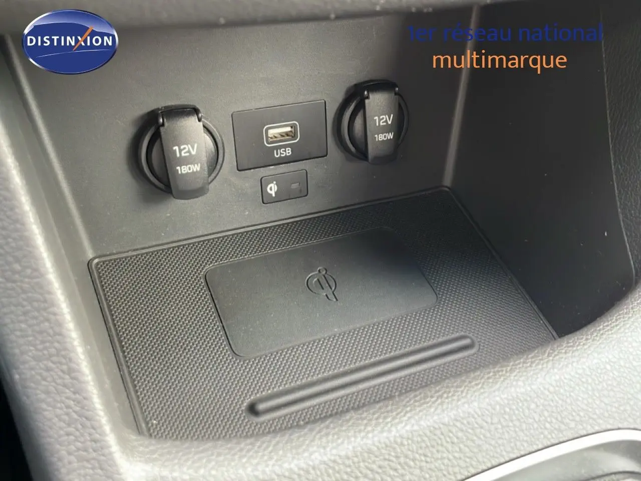 Gros plan sur la console centrale du Hyundai i30 SW blanc, montrant prises 12V, port USB et zone de recharge sans fil.