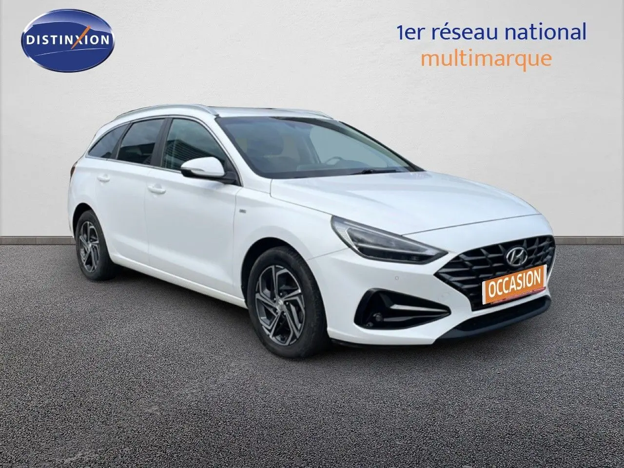 Vue 3/4 avant gauche d'une Hyundai i30 SW 2022 blanche Atlas avec calandre noire et jantes alliage distinctives.
