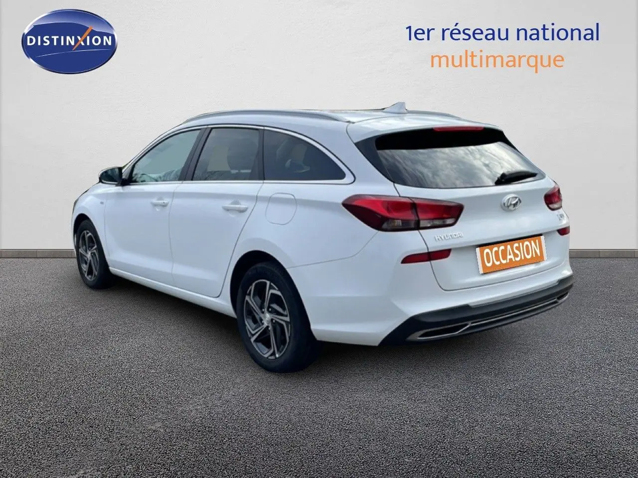 Vue 3/4 arrière droite d'une Hyundai i30 SW blanche Atlas, break compact avec feux arrière rouges et jantes alliage.