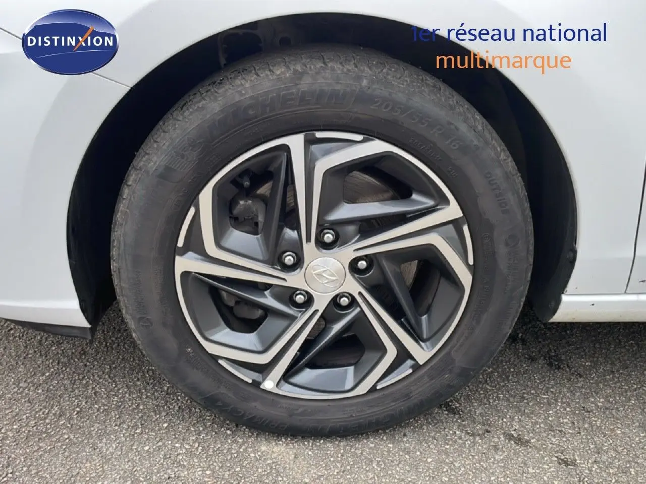 Gros plan sur la roue avant gauche d'une Hyundai i30 SW blanche, avec jante alliage au design géométrique moderne.