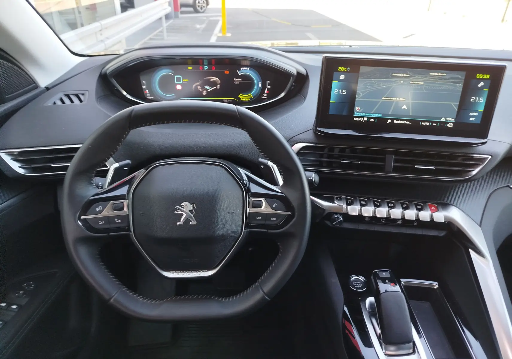 Vue intérieure centrée sur le volant et le tableau de bord numérique d'une Peugeot 3008 hybride, ambiance moderne noire.
