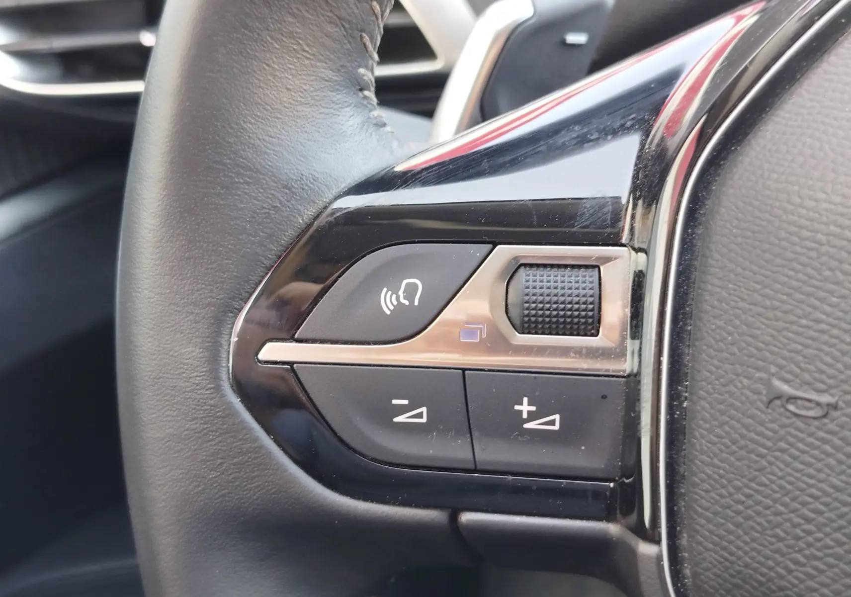 Gros plan sur les commandes du volant noir du Peugeot 3008 Hybrid 225ch, boutons de volume et commande vocale visibles.