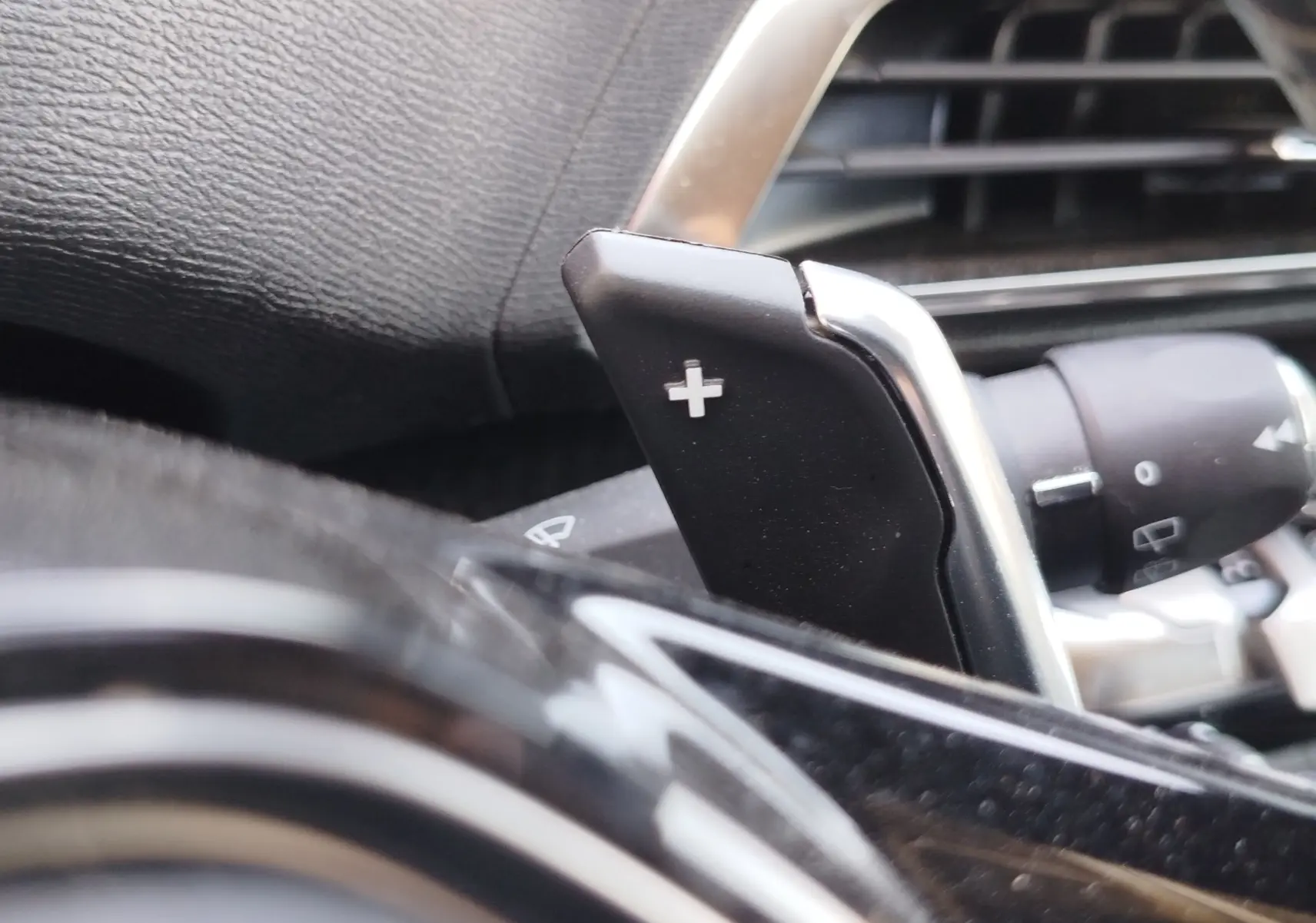 Gros plan sur la palette de changement de vitesse + au volant noir du Peugeot 3008 Hybrid 225ch 2022, intérieur moderne.