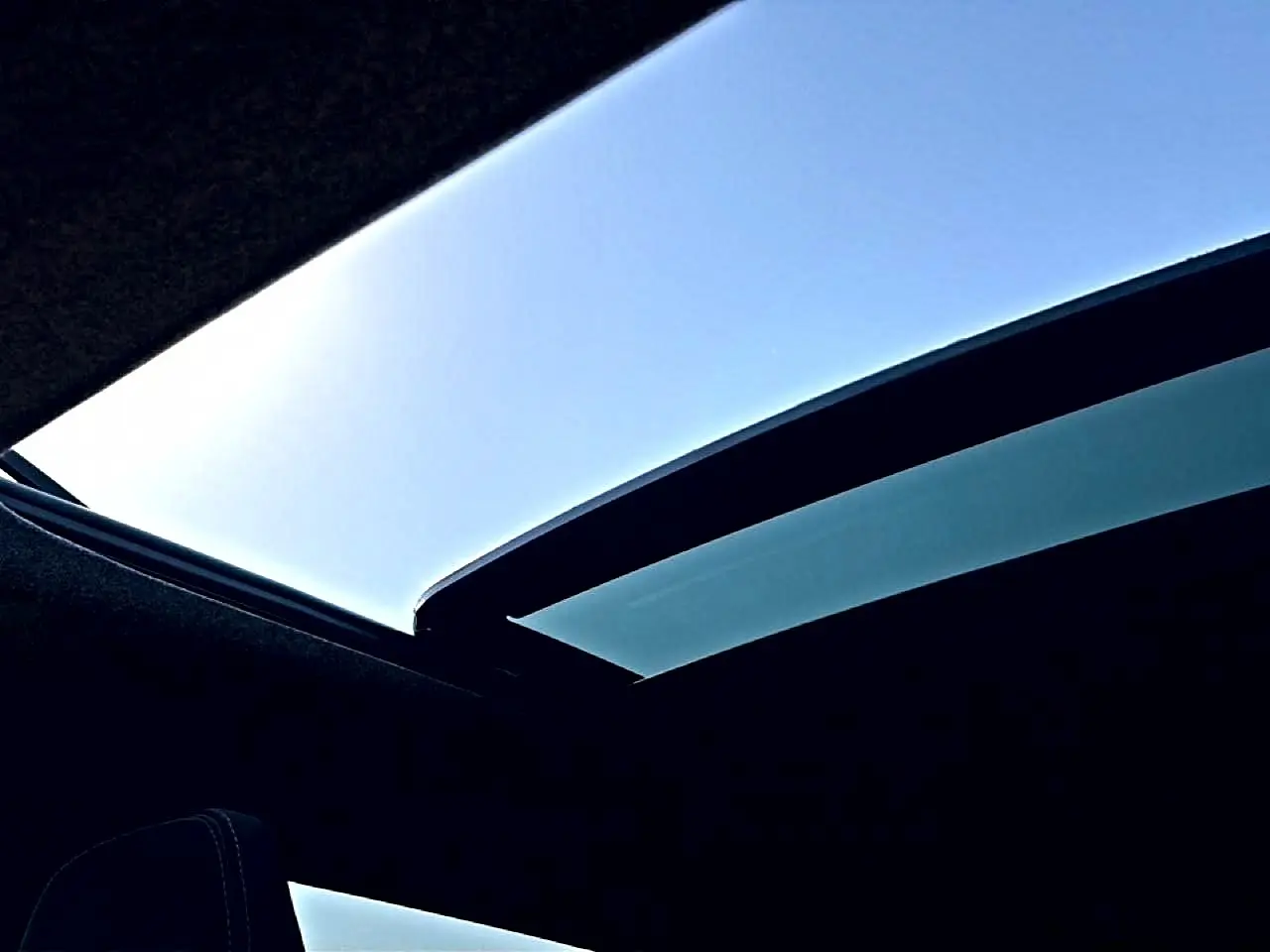 Toit panoramique en verre ouvert du Dacia Bigster blanc, vue intérieure vers le ciel bleu.