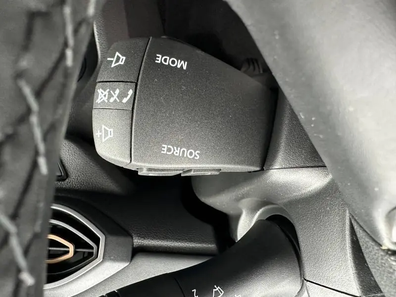 Gros plan sur la commande audio au volant du Dacia Jogger 2024, finition brun Terracota, boutons mode et source visibles.