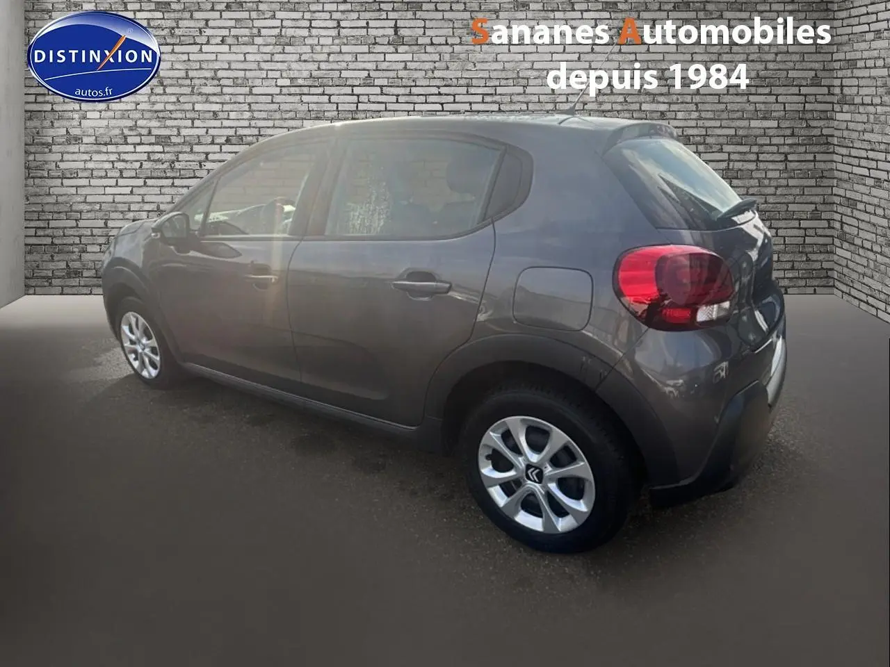 Citroën C3 gris foncé vue de profil côté gauche, stationnée devant un mur en briques grises.