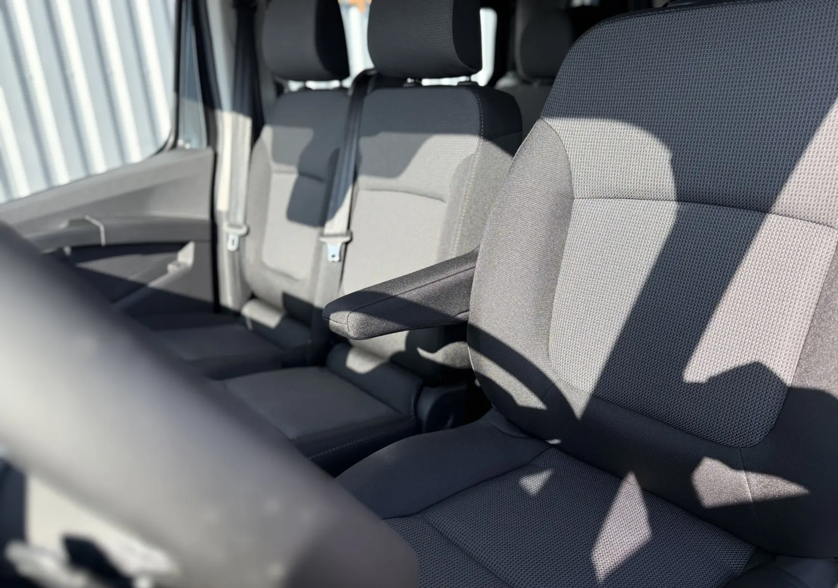 Vue rapprochée des sièges avant en tissu gris du Renault Trafic Cabine Approfondie noir, avec accoudoir côté droit visible.