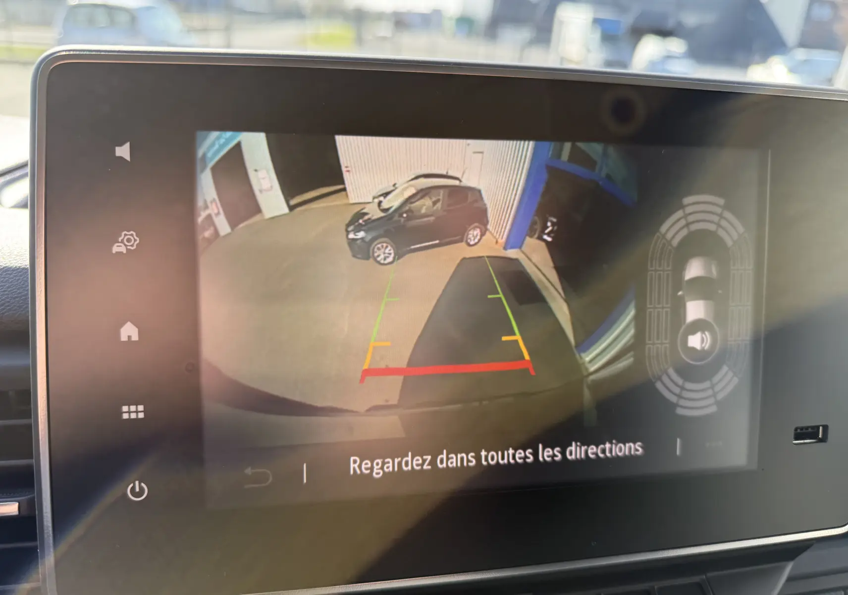 Vue écran caméra de recul montrant une voiture noire garée de profil droit devant un bâtiment industriel.