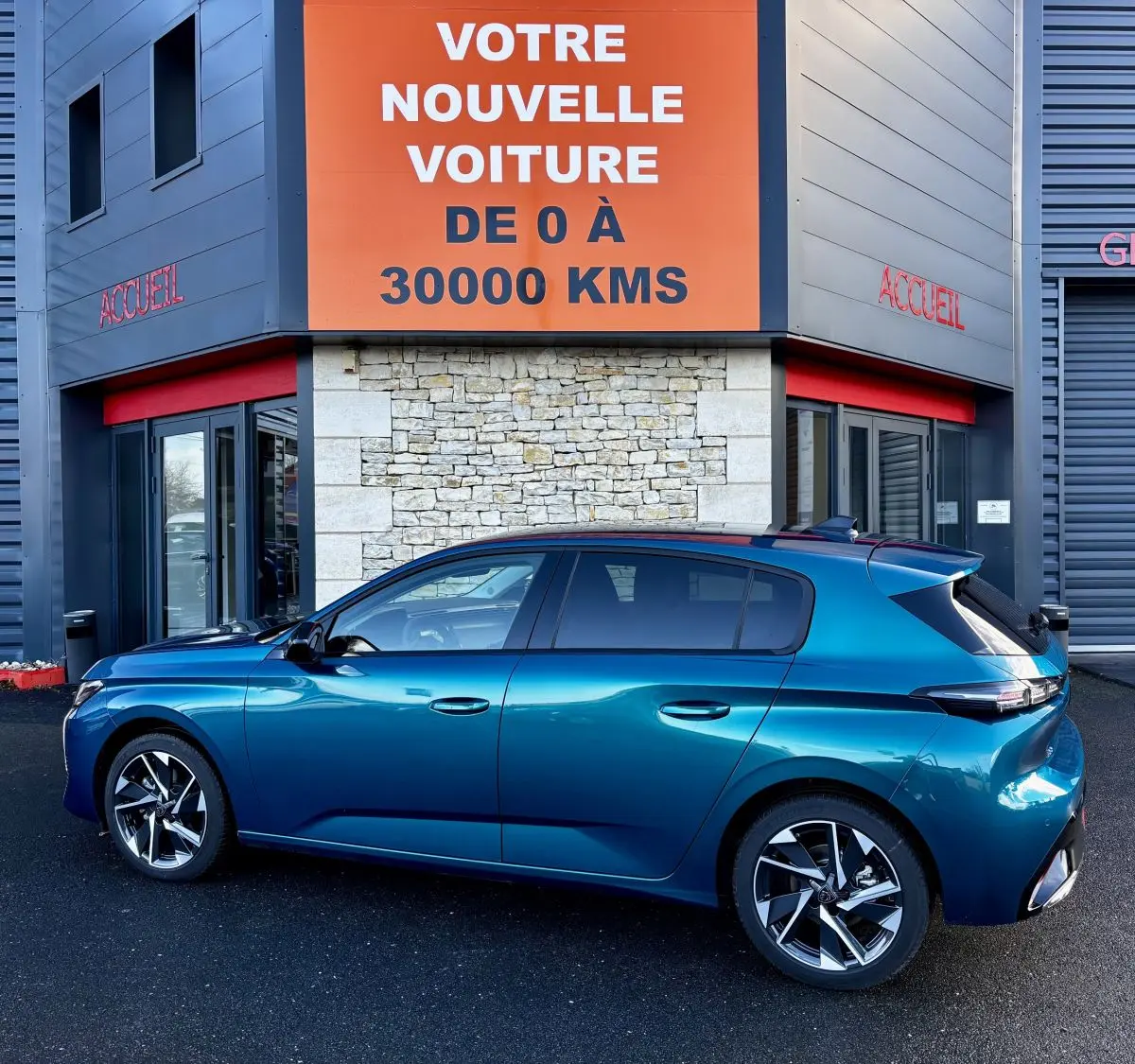 Peugeot 308 Hybrid 136 e-DCS6 Allure bleu vue de profil côté gauche devant un bâtiment avec panneau orange "Votre nouvelle voiture".