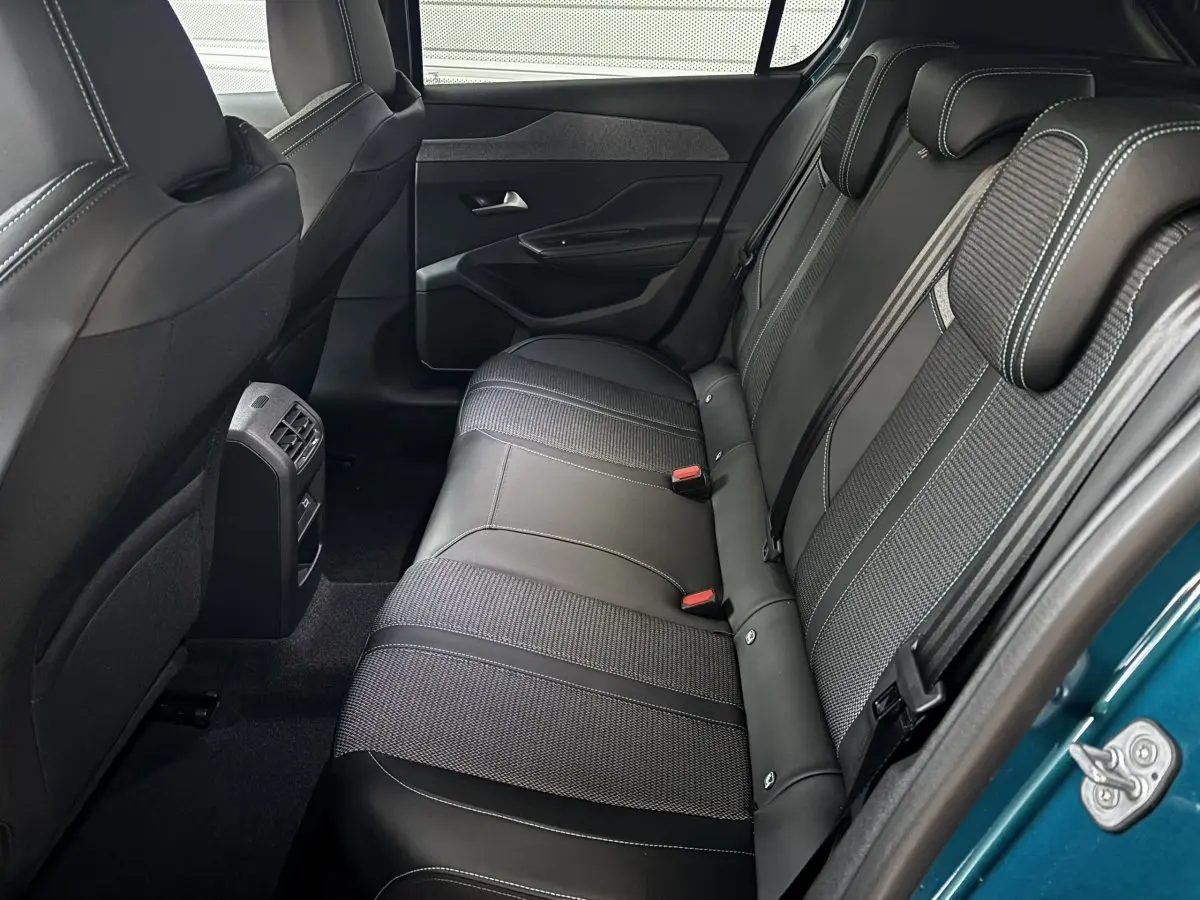 Vue intérieure côté arrière droit de la banquette en cuir noir et tissu de la Peugeot 308 Hybrid 2025 bleu visible à l'ouverture de porte.