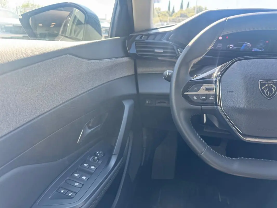 Vue intérieure côté conducteur de la Peugeot 308 Hybrid gris, avec volant multifonction et commandes des vitres électriques.