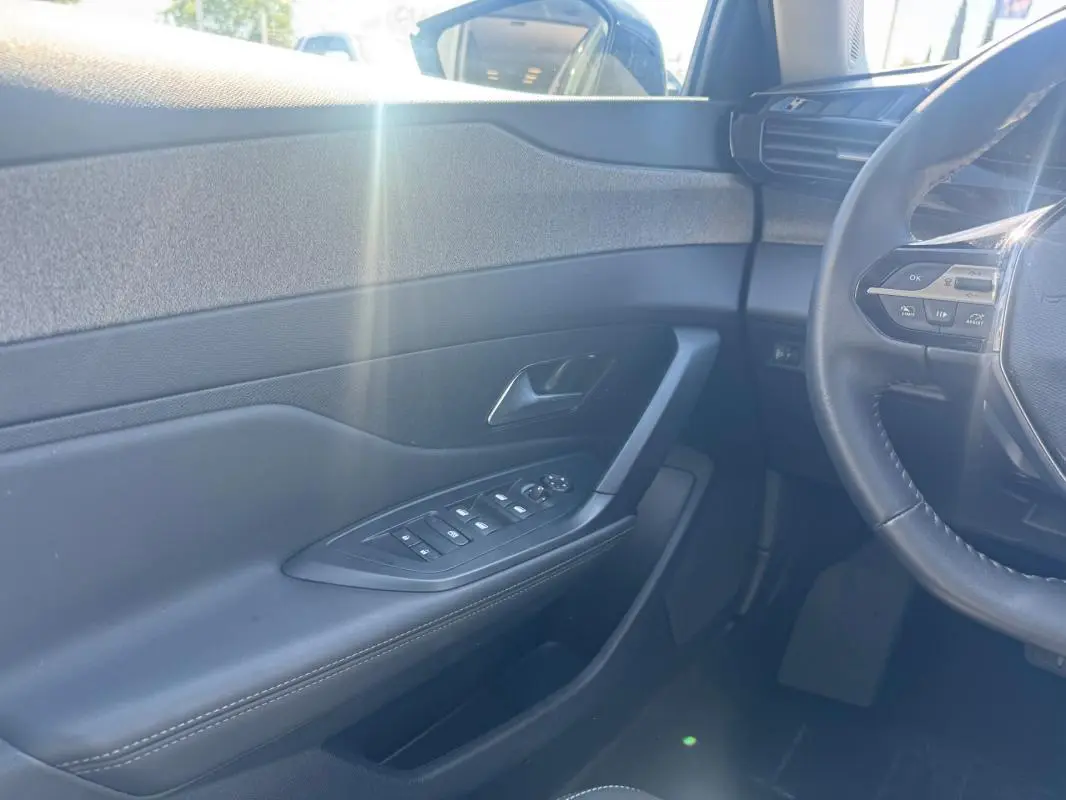 Intérieur côté conducteur d’une Peugeot 308 Hybrid gris, avec porte et commandes électriques, volant partiel et lumière naturelle.