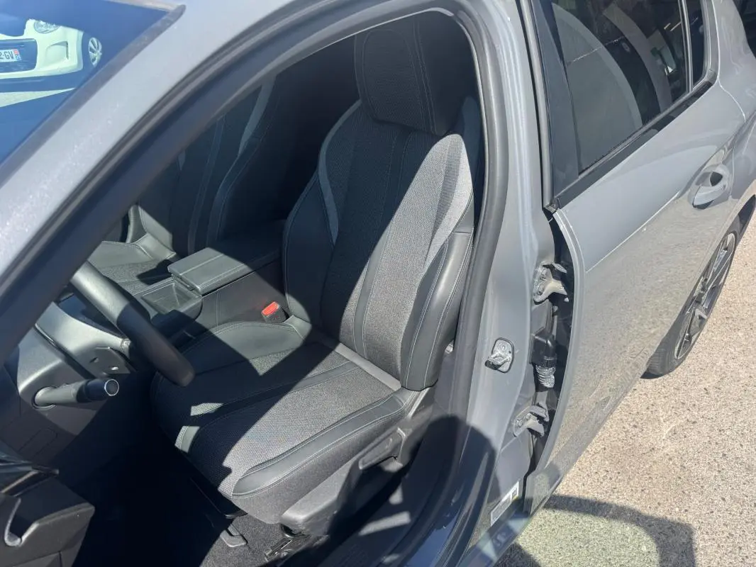 Vue côté conducteur de la Peugeot 308 Hybrid gris 2025, avec siège avant réglable et accoudoir central visible.