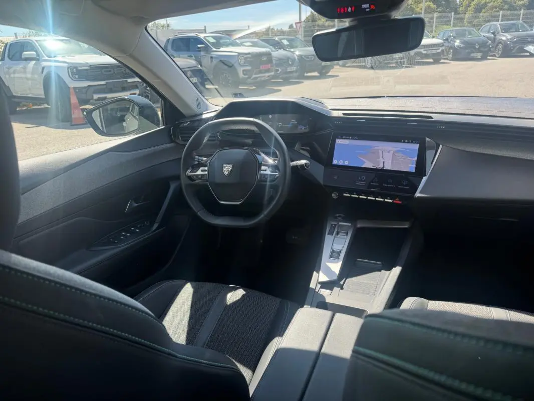 Vue intérieure avant de la Peugeot 308 Hybrid gris, avec volant compact, écran tactile central et cockpit numérique.