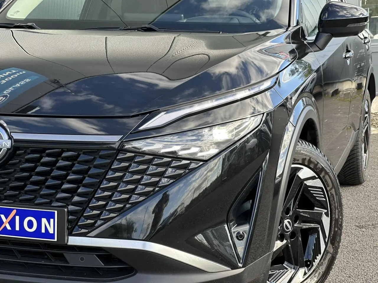 Vue avant droite rapprochée du Nissan Qashqai noir nacré avec calandre distinctive et jantes alliage 18 pouces.