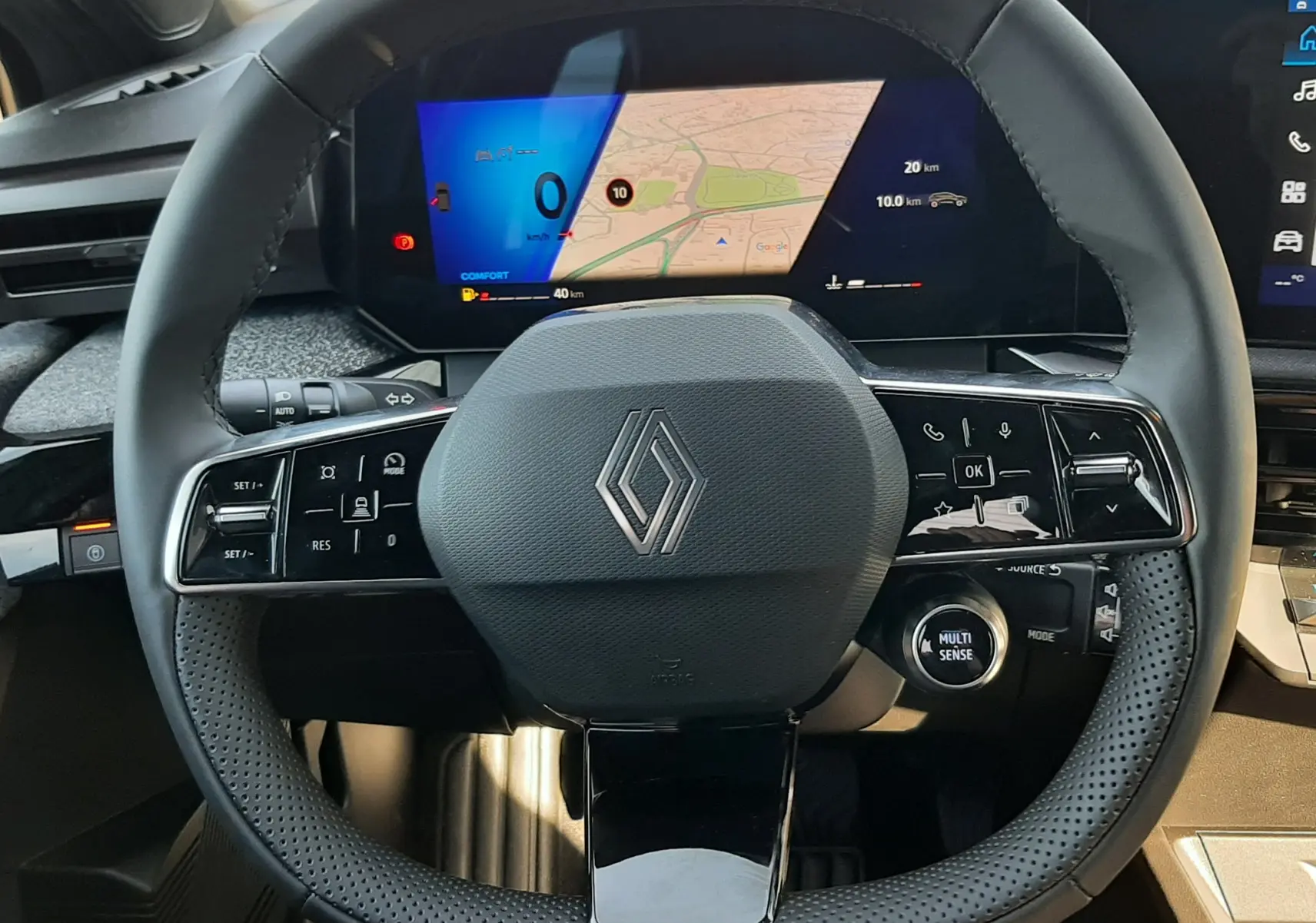 Vue frontale du volant noir perforé de la Renault Clio VI TCe 115ch Techno avec tableau de bord numérique affichant une carte.