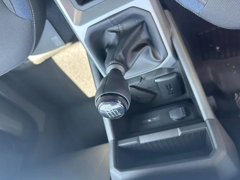 Gros plan sur le levier de vitesses manuel noir du Dacia Duster blanc, avec console centrale et rangements visibles.