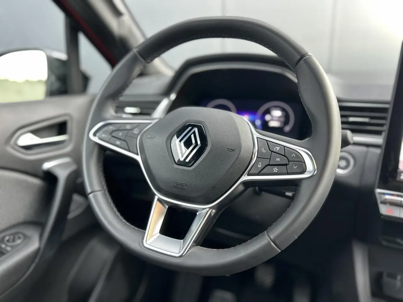 Vue rapprochée du volant noir du Renault Captur 2025, avec commandes intégrées et tableau de bord numérique flou en arrière-plan.