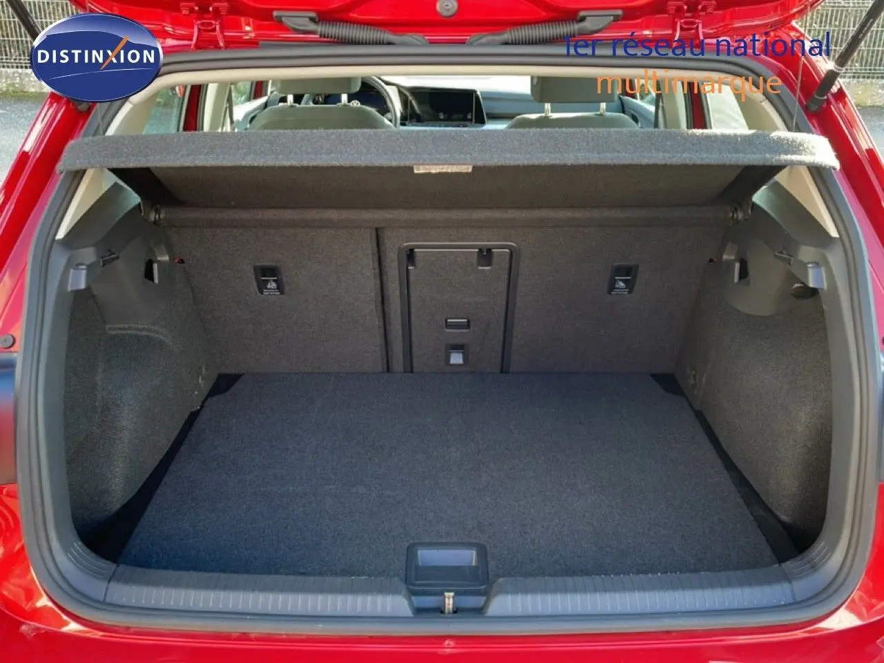 Vue arrière du coffre ouvert d'une Volkswagen Golf VIII rouge Roi Metal, montrant un espace de chargement propre et bien fini.