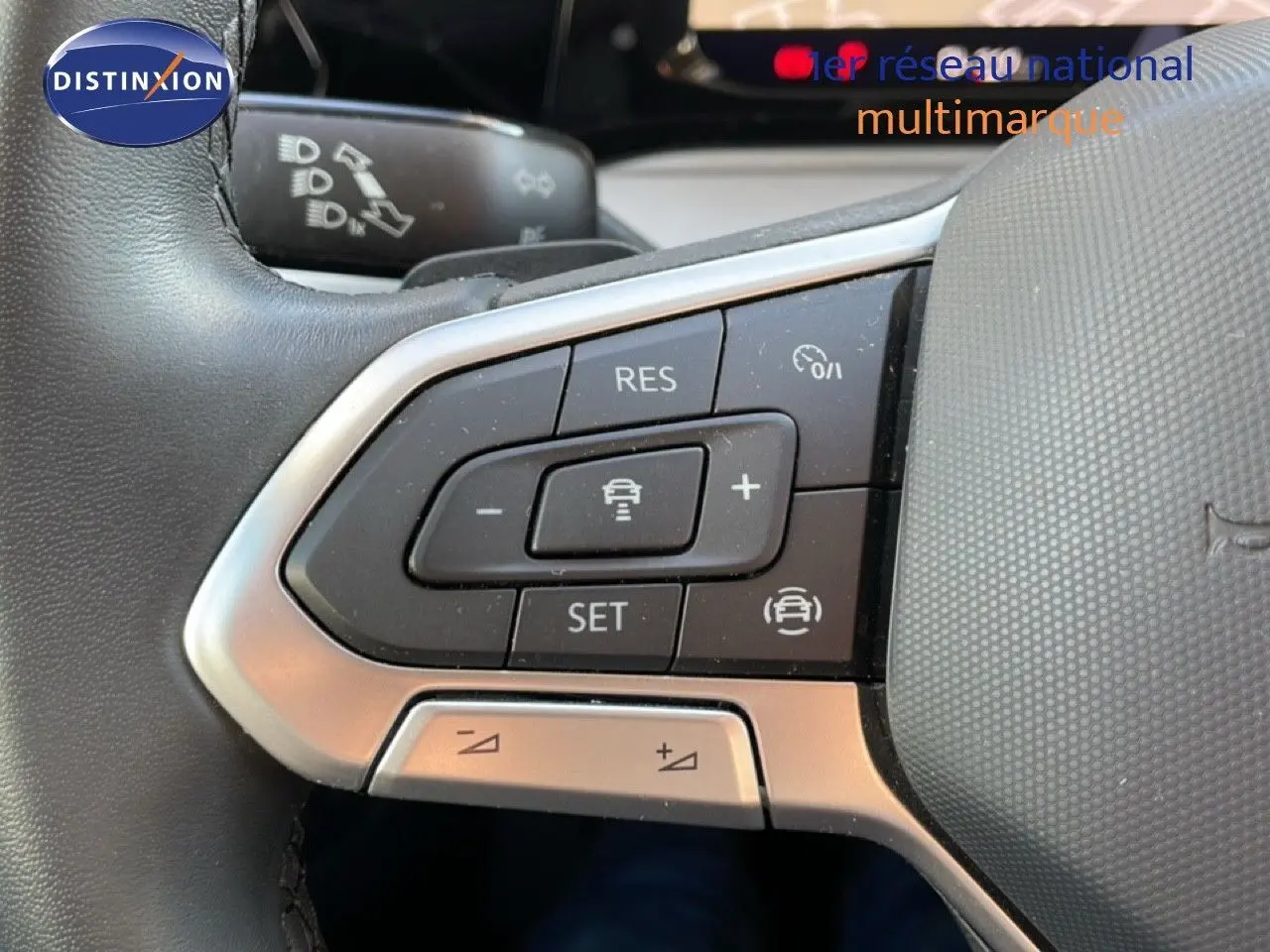 Gros plan sur les commandes au volant côté gauche de la Volkswagen Golf VIII rouge, mettant en valeur les boutons de régulateur de vitesse.