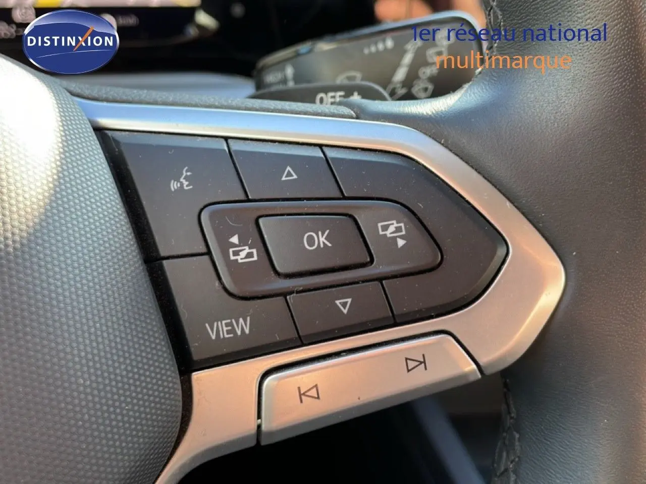 Gros plan sur les commandes multifonctions du volant noir de la Volkswagen Golf VIII rouge Roi Metal, touches OK et navigation visibles.