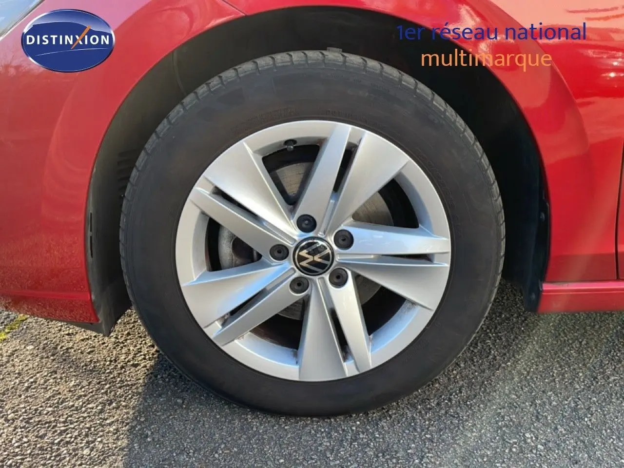 Gros plan sur la roue avant gauche d'une Volkswagen Golf VIII rouge Roi Metal avec jante alliage argentée.