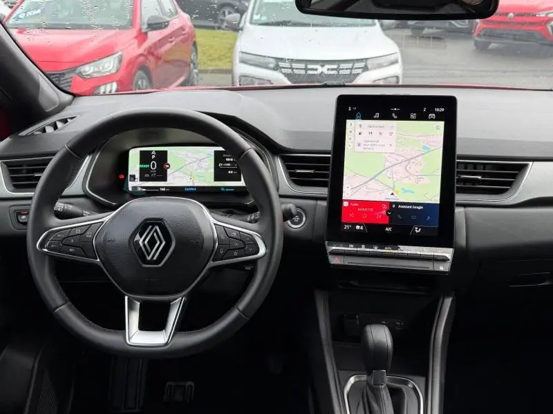 Vue intérieure du tableau de bord du Renault Captur 2025 hybride, avec volant multifonction et écran tactile central vertical.