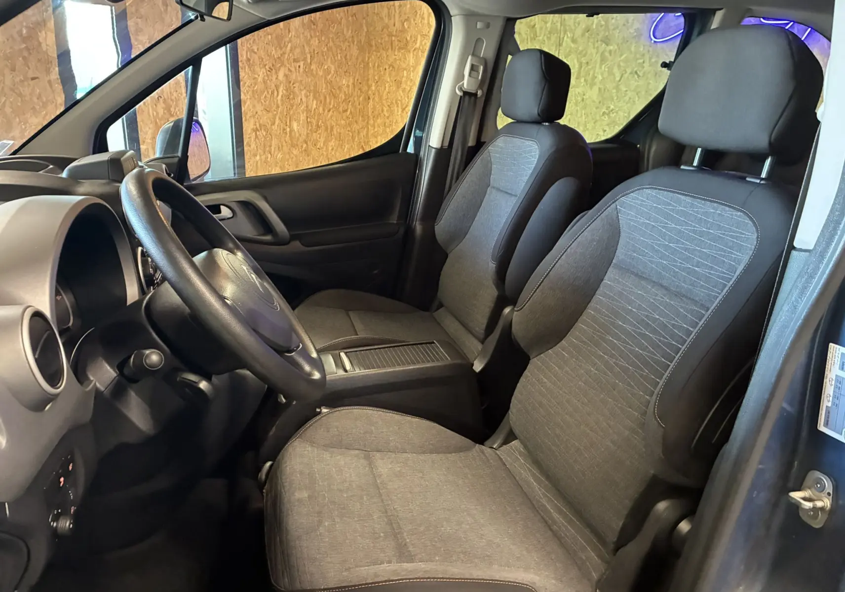 Vue intérieure côté conducteur du Citroën Berlingo Multispace bleu, sièges avant en tissu gris et noir, volant visible.