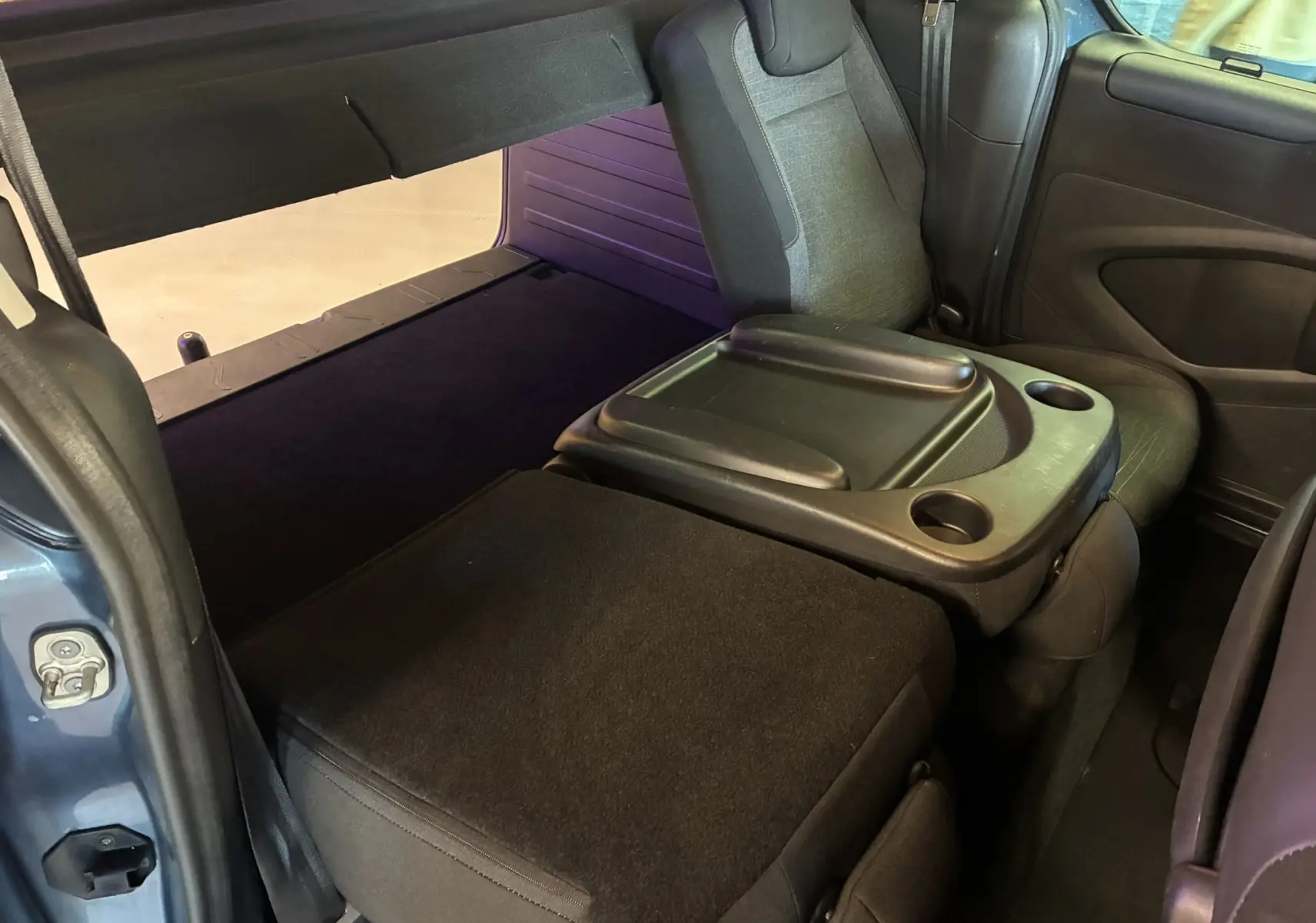 Vue intérieure arrière du Citroën Berlingo Multispace bleu 2017, siège rabattable avec tablette et porte-gobelets intégrés.