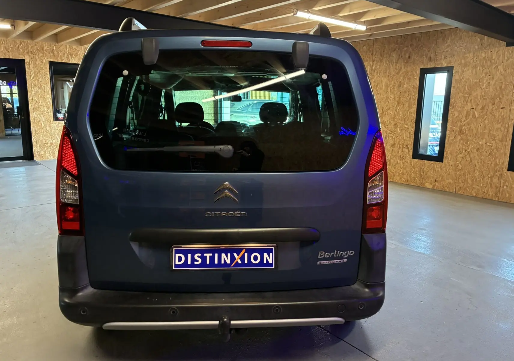 Vue arrière d'un Citroën Berlingo Multispace bleu 2017 avec hayon vitré et feux verticaux rouges dans un garage.