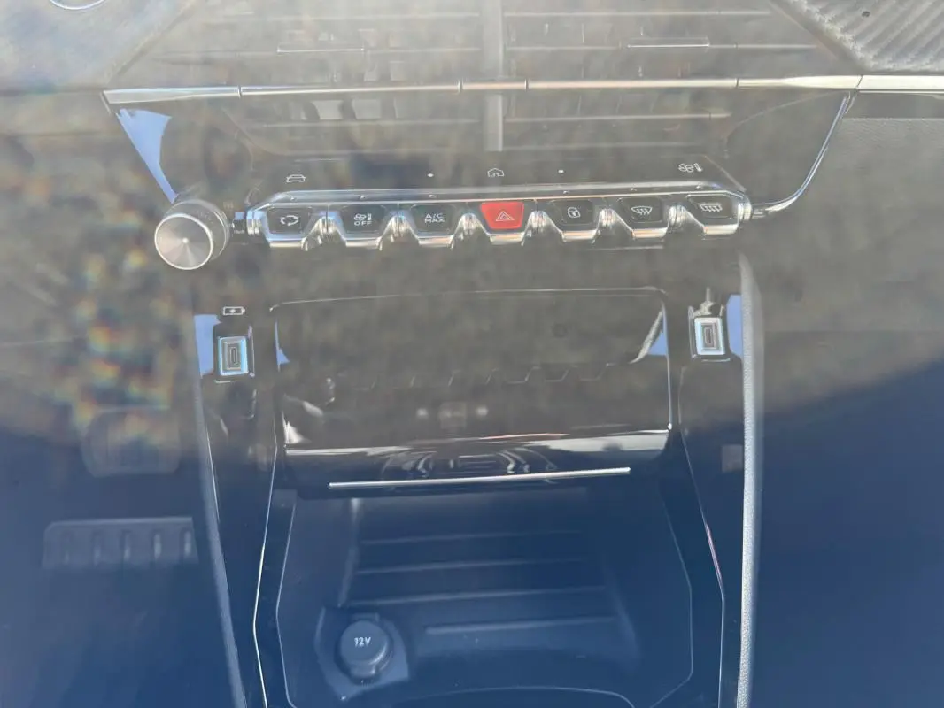 Vue rapprochée de la console centrale du Peugeot 2008 Hybrid 136 Allure 2025 noire, avec commandes et prise 12V visibles.
