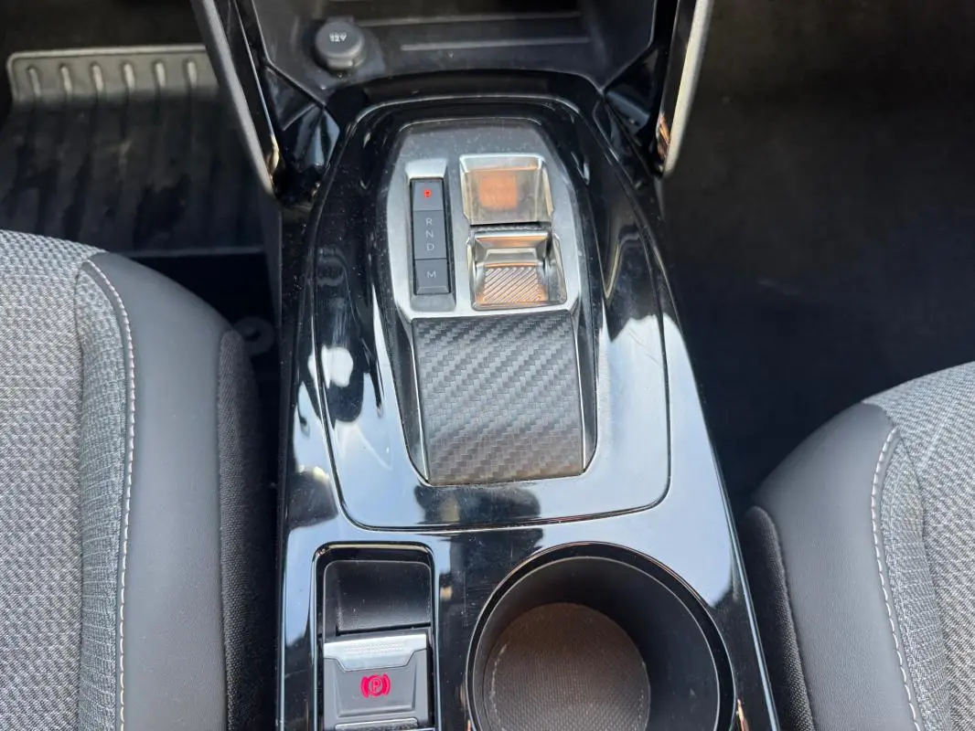 Vue rapprochée de la console centrale noire du Peugeot 2008 Hybrid 136 e-DCS6 Allure avec sélecteur de vitesse et frein à main électrique.