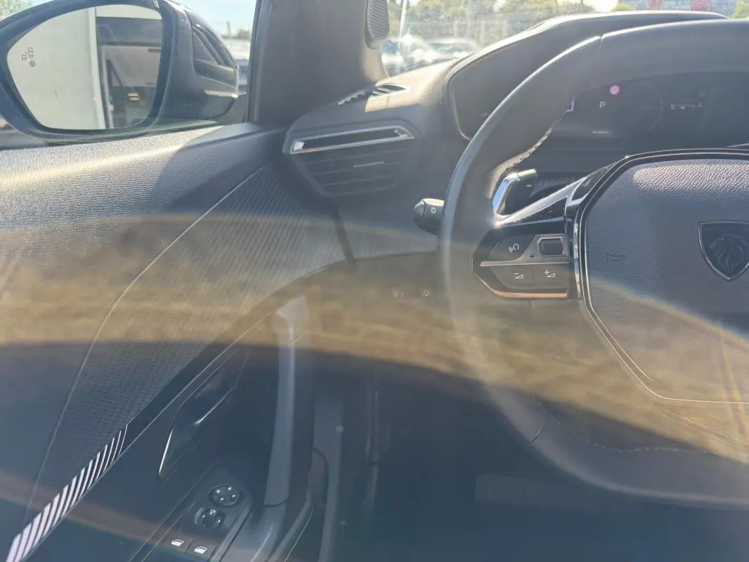 Vue intérieure côté gauche du Peugeot 2008 Hybrid noir 2025, montrant le volant, les commandes de vitres et le rétroviseur dégivrant.
