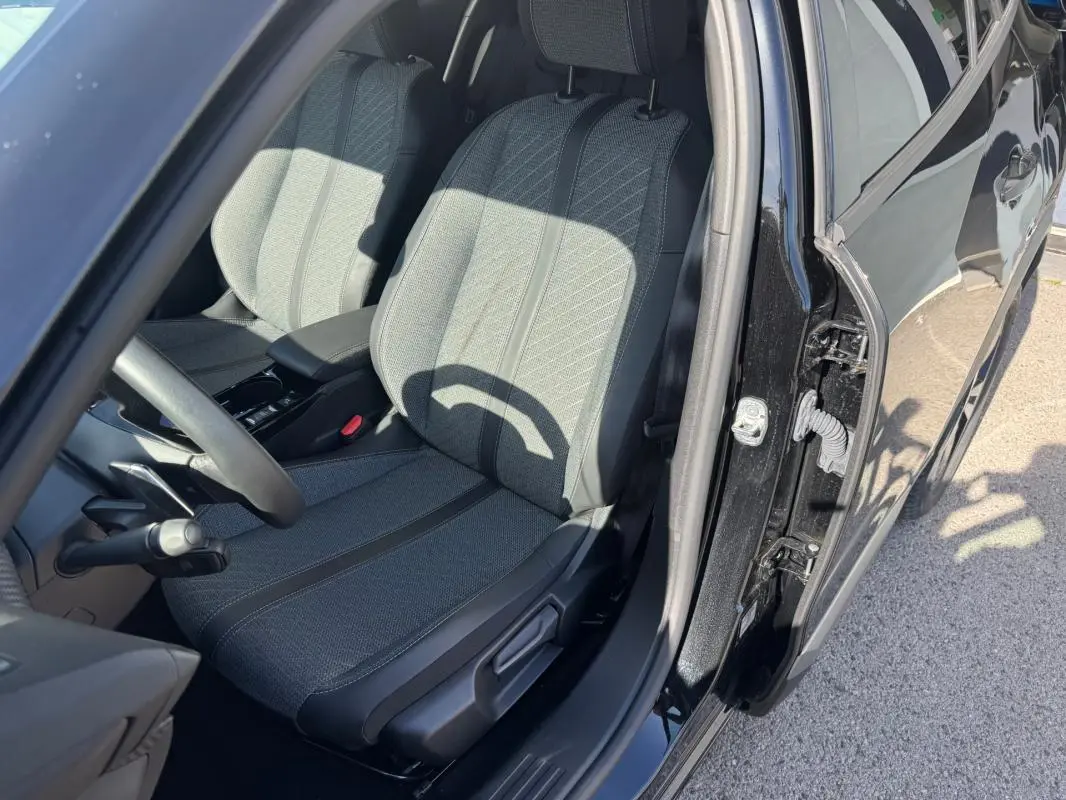 Vue intérieure côté conducteur du Peugeot 2008 Hybrid noir 2025, mettant en valeur le siège avant en tissu et l'ouverture de porte.