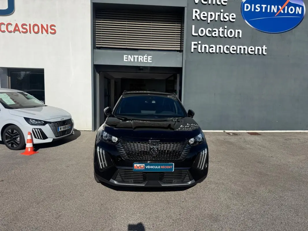 Vue avant d'un Peugeot 2008 Hybrid noir avec barres de toit, stationné devant une concession automobile.