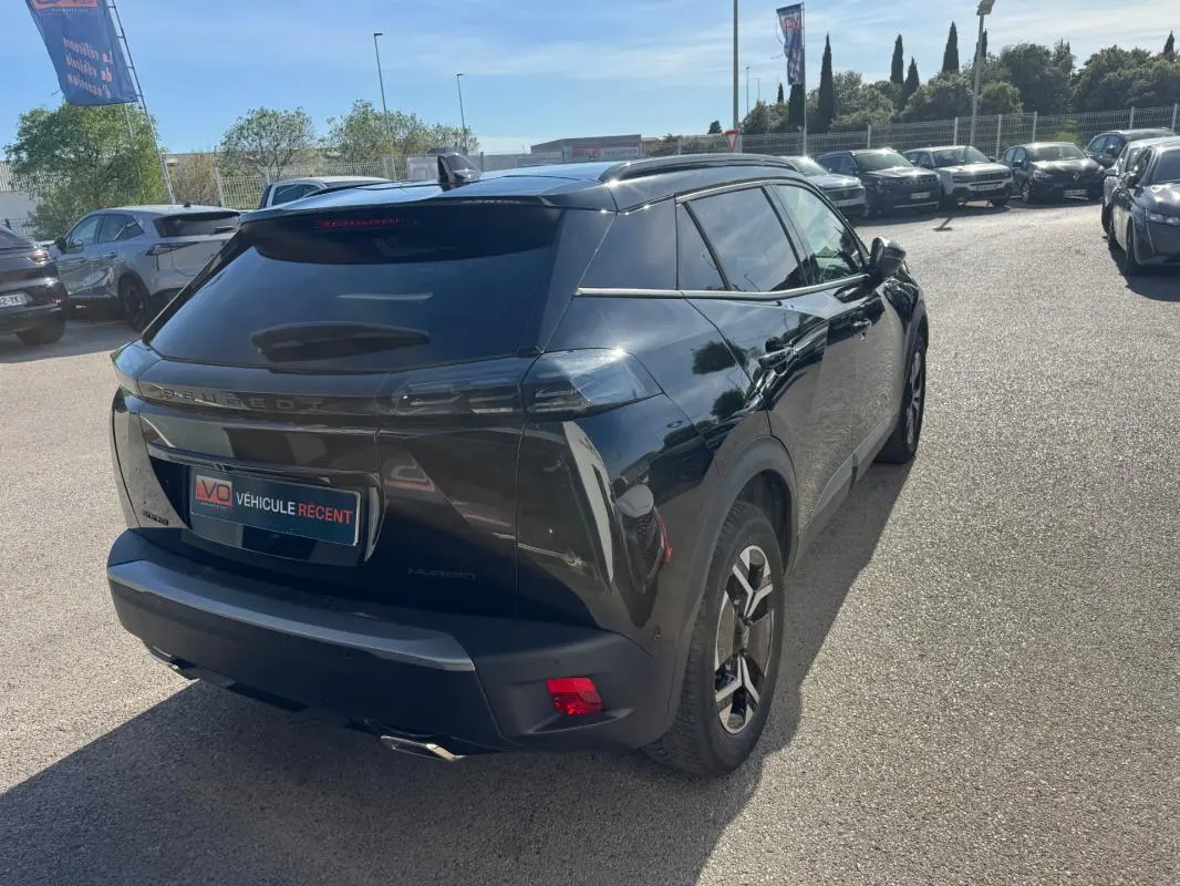 Vue 3/4 arrière droite d’un Peugeot 2008 Hybrid noir avec jantes alliage 17 pouces et barres de toit visibles.