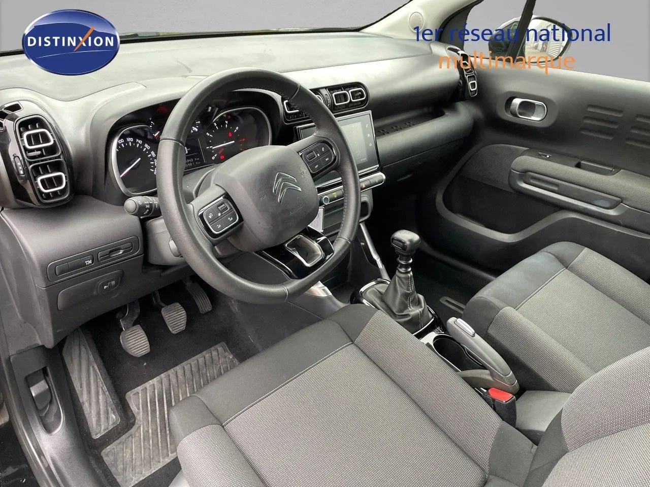Intérieur du Citroën C3 Aircross 2023 en tissu gris, vue côté conducteur avec volant multifonction et boîte manuelle.