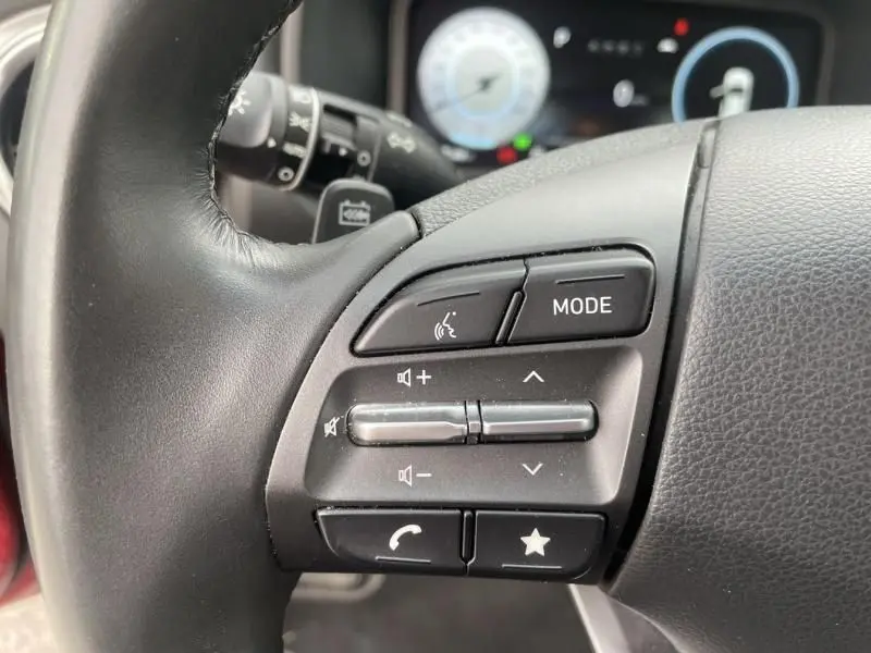 Gros plan sur les commandes au volant côté gauche du Hyundai Kona électrique rouge métal 2021, avec boutons audio et téléphone.